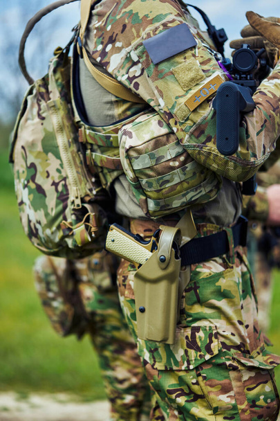 Großaufnahme einer Pistole im Holster und einer Maschinenpistole in den Händen eines Soldaten in Militäruniform - Foto, Bild