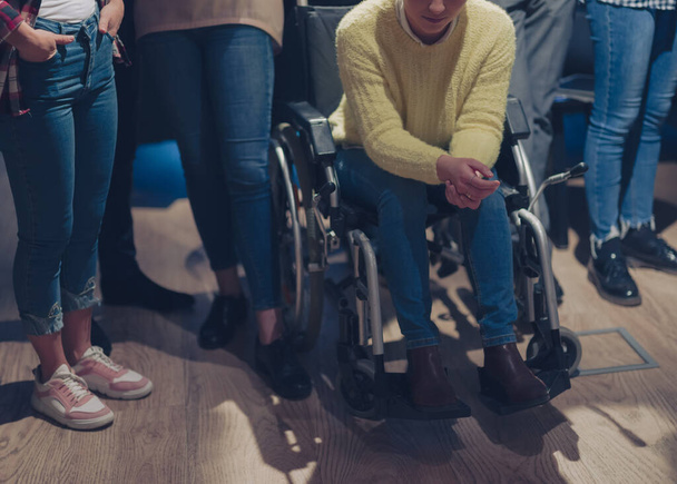Sad and depressed disabled businesswoman in a wheelchair at the office with coworkers. Diverse business team in a modern open space coworking office space. High quality photo - Φωτογραφία, εικόνα