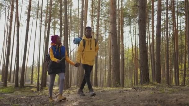 Een jong stel zwarte mannen en vrouwen lopen in het bos tijdens een reis naar het bos met rugzakken in slow motion. Twee Afrikanen lopen door het bos met rugzakken tijdens het toerisme - Video