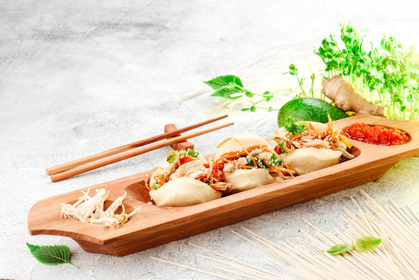 Tradycyjne potrawy panazjatyckie. Bao - ciasto na parze z nadzieniem mięsnym i świeżych warzyw na drewnianym talerzu z chińskimi pałeczkami. Konkretne tło. Miejsce na tekst - Zdjęcie, obraz