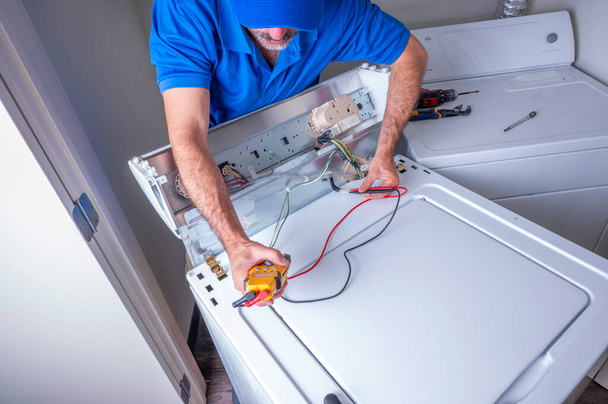 Technicien ou réparateur d'appareils travaillant sur des circuits pour une machine à laver à charge maximale à l'intérieur d'une maison résidentielle - Photo, image