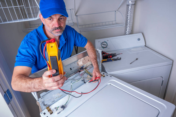 Un técnico de electrodomésticos probando circuitos en una lavadora residencial, en uniforme, mirando el voltímetro - Foto, Imagen