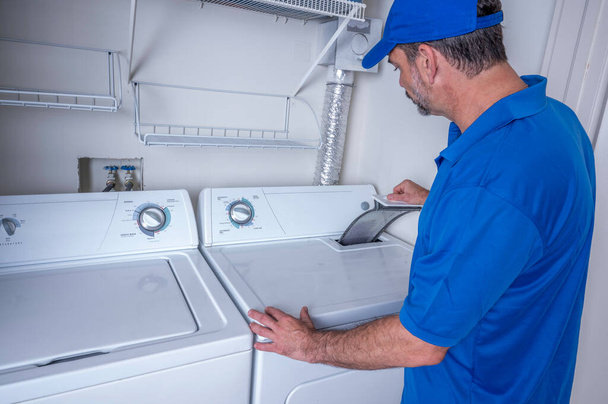 Técnico de eletrodomésticos profissional verificando uma armadilha de fiapos em um secador residencial - Foto, Imagem