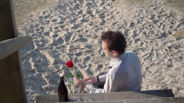Een man wacht op een meisje op een date, kijkt nerveus op zijn horloge, hij draagt een shirt en een joggingbroek, het concept van een ontmoeting en een date, wachtend - Video