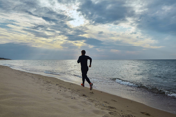 Young man in sports outfit runs along the seashore - Фото, зображення