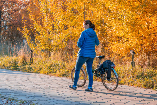 Kazan, Russia - October 03, 2020: A woman walks next to her bike in a city park on a sunny autumn day - Fotó, kép