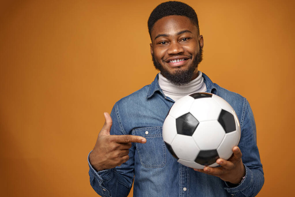 African american man holding soccer ball and pointing on it, yellow background - Foto, immagini
