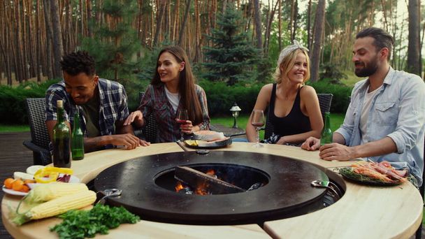 Amici gioiosi rilassarsi vicino barbecue grill. Persone positive trascorrere del tempo nel fine settimana - Foto, immagini