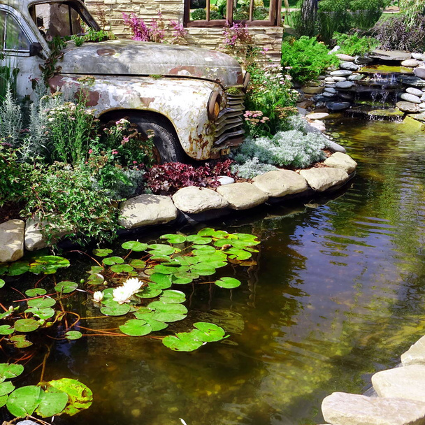 デザイン要素としてPVCと古い車から小さな人工池と現代的な造園裏庭の庭。装飾池と古い車と石造りの風景レトロなスタイルと家の中のモダンな庭. - 写真・画像