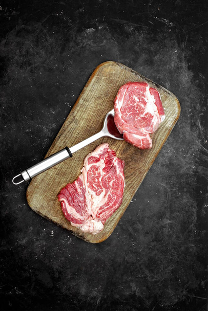 Raw Marbled Loin Beef Steaks and Grill Tools On Wooden Cutting Board Beef Steaks On Spatula Ready for BBQ or Grilling, Overhead View (англійською). Raw Striploin Marbled Beef Steaks on Black Background, Top View. - Фото, зображення