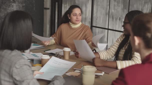 За плечами неузнаваемых офисных работников, смотрящих на эмоциональную смешанную расу женщину, выражающую замешательство по поводу данных в деловых бумагах, рассказывающую об этом коллегам - Кадры, видео