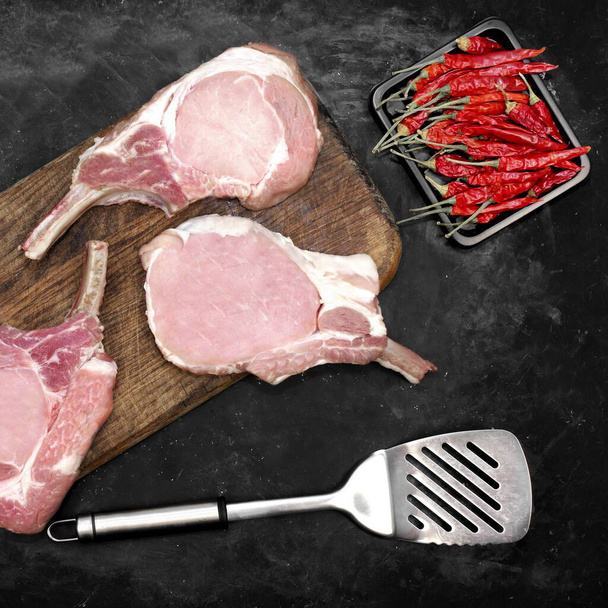 Schweinefleisch-Ribeye-Steaks zum Grillen oder Braten und Kochen auf schwarzem Hintergrund, Overhead View. Tomahawk Pork Steaks auf Schneidebrett, Draufsicht. Rohe Schweineknochensteaks auf schwarzem Hintergrund, Draufsicht. - Foto, Bild