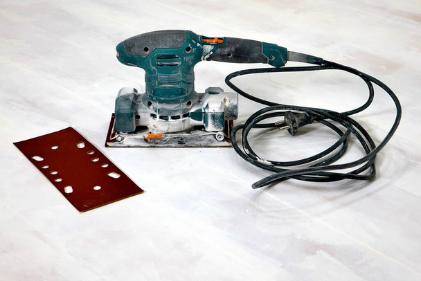 Elektrische schuurmachine op de houten vloer met schuurpapier - Foto, afbeelding