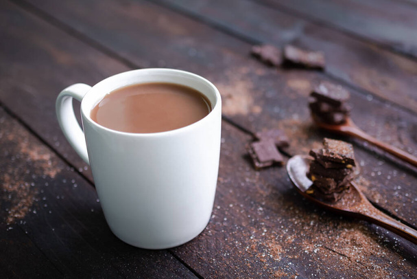 Csokoládé tej fehér csésze bárcsokoládé kanállal fa asztal háttér. Kókusz forró ital reggel az egészségért. Csokoládé világnap és snack vagy reggeli koncepció. - Fotó, kép