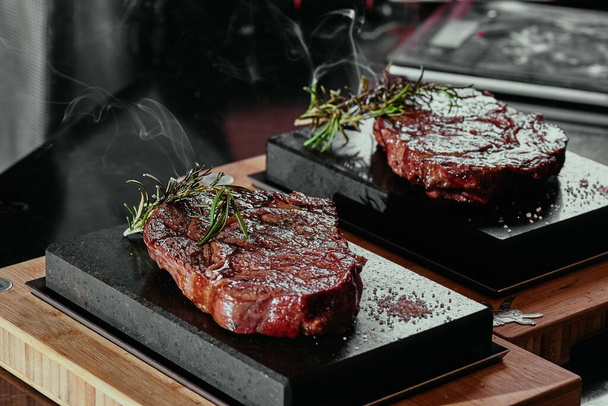Erjesztett steak. Ribeye steak egy négyzet alakú fekete kő tányéron. Zárj be! sötét háttér - Fotó, kép