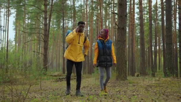 Két afro-amerikai túrázó hátizsákkal, akik az erdőben sétálnak, miközben a tájat nézik. Pár fekete férfi és nő vesz mobiltelefon utazás felfedezés vad erdők természet csapatban - Felvétel, videó