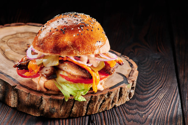 Burger met kip, kaas, tomaten, rode uien en sla op houten snit op zwarte achtergrond. Burger menu. Ruimte voor tekst. Ongezond voedsel - Foto, afbeelding