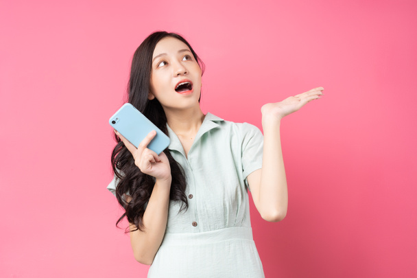 Joven mujer asiática sosteniendo el teléfono y mirando hacia arriba con emoción - Foto, Imagen