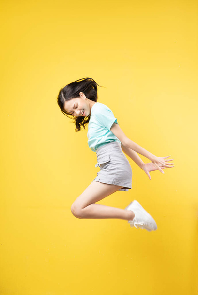 Young Asian girl jumping on yellow baclground - Foto, afbeelding