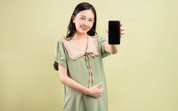 Pregnant Asian woman holding phone in hand - Foto, Imagen