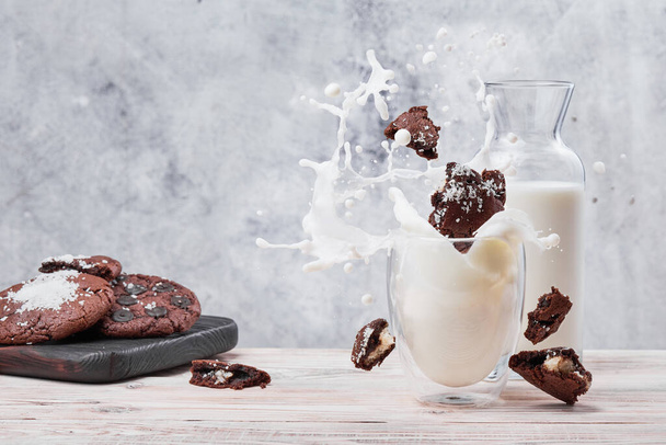 Splash of vegan milk in transparent glass. Chocolate cookies and glass of milk on light concrete background. Space for text - Zdjęcie, obraz