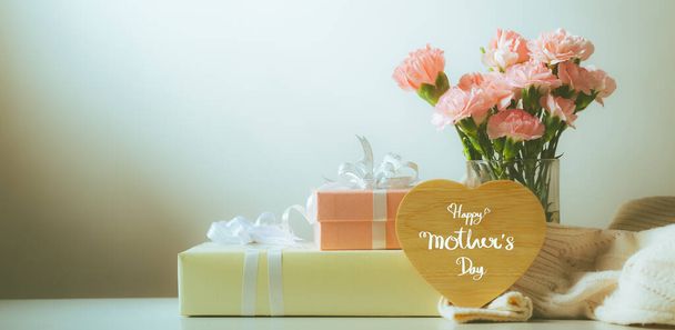 Νεκρή φύση με γλυκά άνθη γαρύφαλλου και δώρο στο τραπέζι, έννοια Ημέρα της Μητέρας, Vintage χρώμα φίλτρου - Φωτογραφία, εικόνα