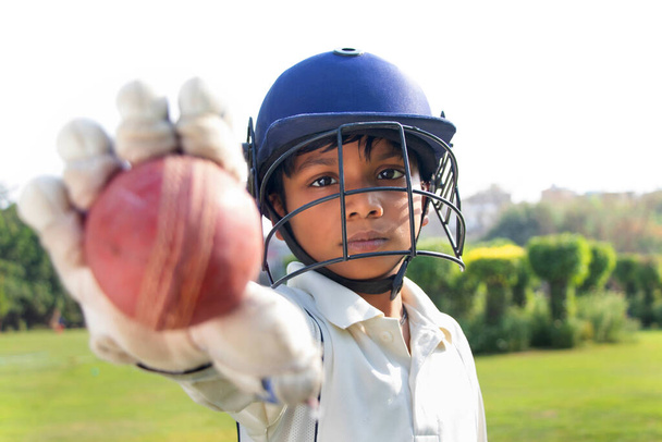 Porträt eines Jungen, der Crickethelm trägt und Cricketball zeigt - Foto, Bild