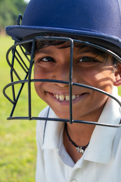 Portrait of boy wearing cricket helmet and smiling - 写真・画像