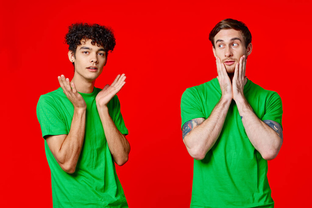 двое мужчин, держащих головы в зеленых футболках на красном фоне - Фото, изображение