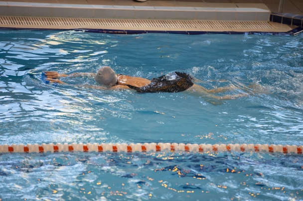 Kobieta pływa w czarnym stroju kąpielowym i czapce kąpielowej pływa w basenie. - Zdjęcie, obraz