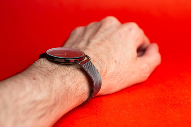 reloj de pulsera con la mano de un hombre sobre fondo rojo. - Foto, imagen