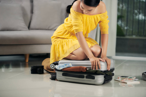 Low section of woman kneeling on overstuffed suitcase in floor - Photo, Image
