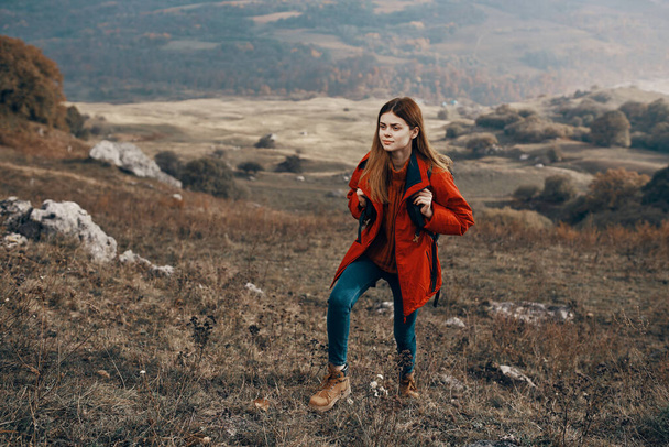 Sırt çantalı ceketli bir kadın yürüyüşçü dağ manzarasında seyahat ediyor. - Fotoğraf, Görsel