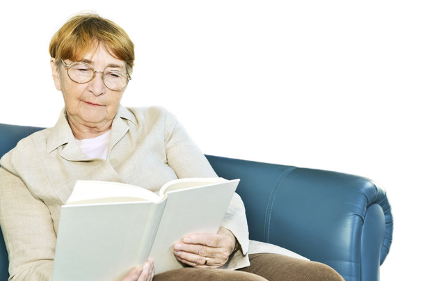 Elderly woman relaxing on couch reading a book - Фото, изображение