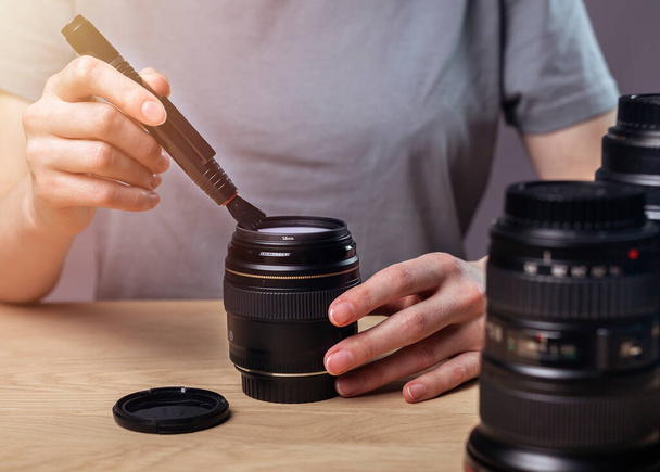 Female hands clean digital camera lens with professional brush, removing dust. - Фото, зображення