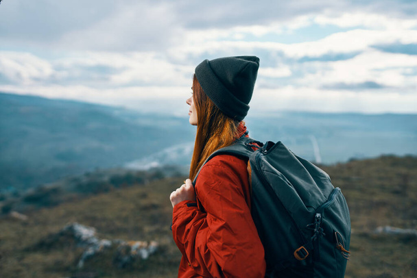 mujer chaqueta sombreros mirando a la montaña en la distancia azul cielo nubes modelo mochila - Foto, Imagen