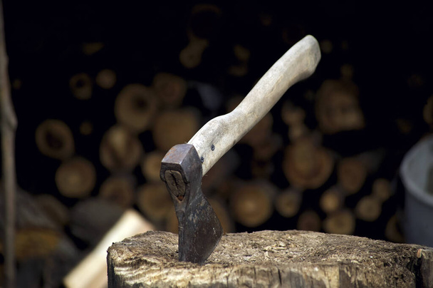 el hacha está atascada en un tronco cerca de la pila de madera, en la primavera - Foto, Imagen