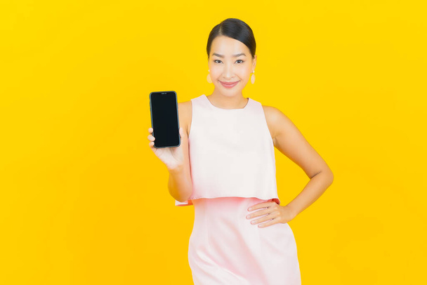 Портрет красива молода азіатка посміхається зі смартфоном на жовтому кольоровому фоні
 - Фото, зображення