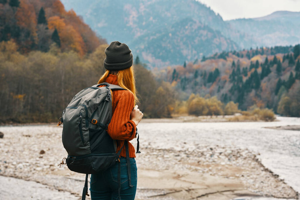mujer viaja en las montañas en otoño cerca del río en la naturaleza con una mochila vista trasera - Foto, imagen