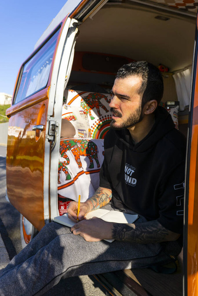 A vertical shot of a Caucasian male with tattoos in a studio-furnished van - Foto, Bild
