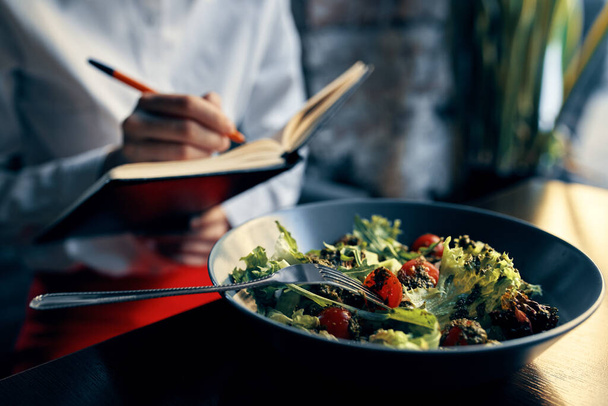jegyzettömb tollal a kezében és saláta egy tányéron étterem kávézó felirattal - Fotó, kép