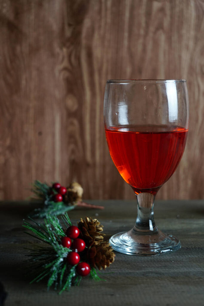 A vertical shot of a glass of red wine on the table with decorative holly berries on it - 写真・画像