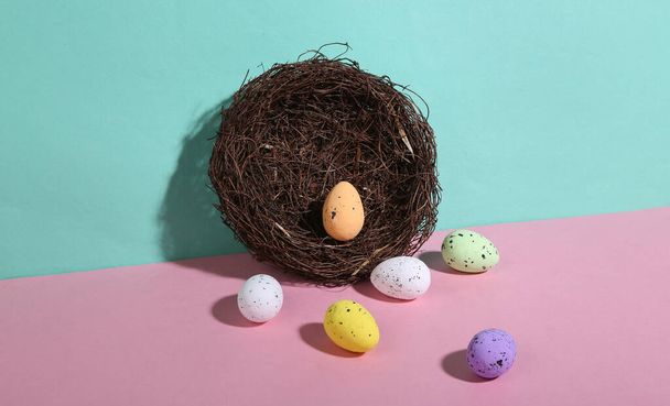 Nest with colored Easter eggs on blue-pink pastel background. Minimalism. Trendy shadow. Creative layout. - Fotó, kép