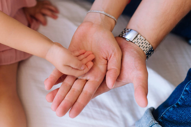 Παιδικό χέρι στην παλάμη της μητέρας και του πατέρα σε λευκό φόντο. Συμβολίζει την οικογενειακή υποστήριξη. Γυναικεία, ανδρικά και παιδικά χέρια τοποθετούνται παλάμες προς τα πάνω. - Φωτογραφία, εικόνα