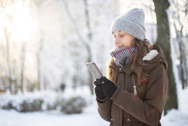 Mladá atraktivní žena v teplém oblečení pomocí smartphone v zimě zasněžené počasí - Fotografie, Obrázek