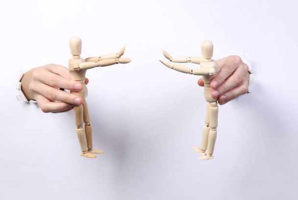 Kobiece ręce trzymające drewniane kukiełki przez podarty, dziurkowany, biały papier. Władca Marionetek. Minimalizm - Zdjęcie, obraz