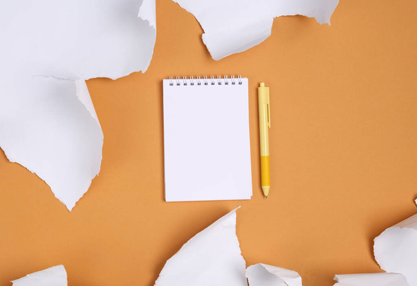 Cuaderno y hojas de papel blanco desgarrado sobre fondo beige. Vista superior - Foto, imagen