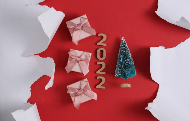 Подарочные коробки с мини елкой и белым порванным листом бумаги на красном фоне. 2022 новый год. Рождество, праздничный фон. - Фото, изображение