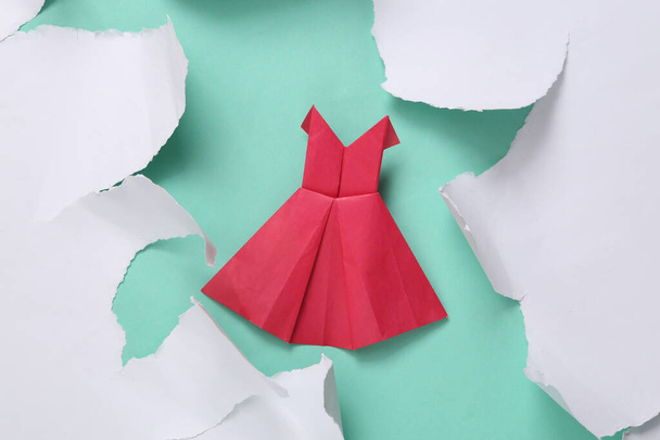 Origami-Kleid auf blauem Hintergrund mit weißem zerrissenen Papier. Modekonzept. Minimalismus. Ansicht von oben - Foto, Bild