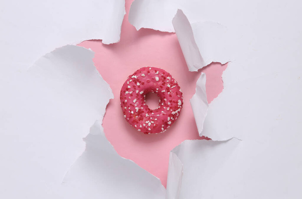 Köstlicher süßer Donut durch das aufgerissene Loch des Papiers. Konzeptkunst. Minimalismus - Foto, Bild